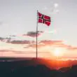 Det norske flagg som flagrer i vinden, med en solnedgang i bakgrunnen.
