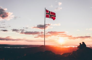 Det norske flagg som flagrer i vinden, med en solnedgang i bakgrunnen.