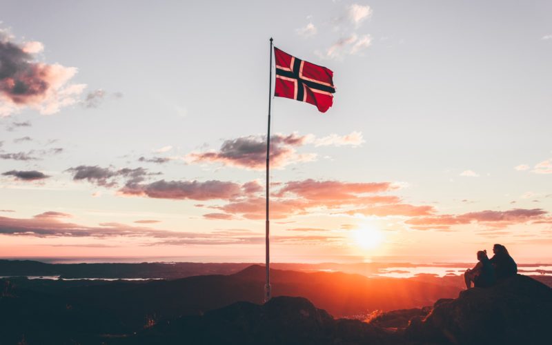 Det norske flagg som flagrer i vinden, med en solnedgang i bakgrunnen.